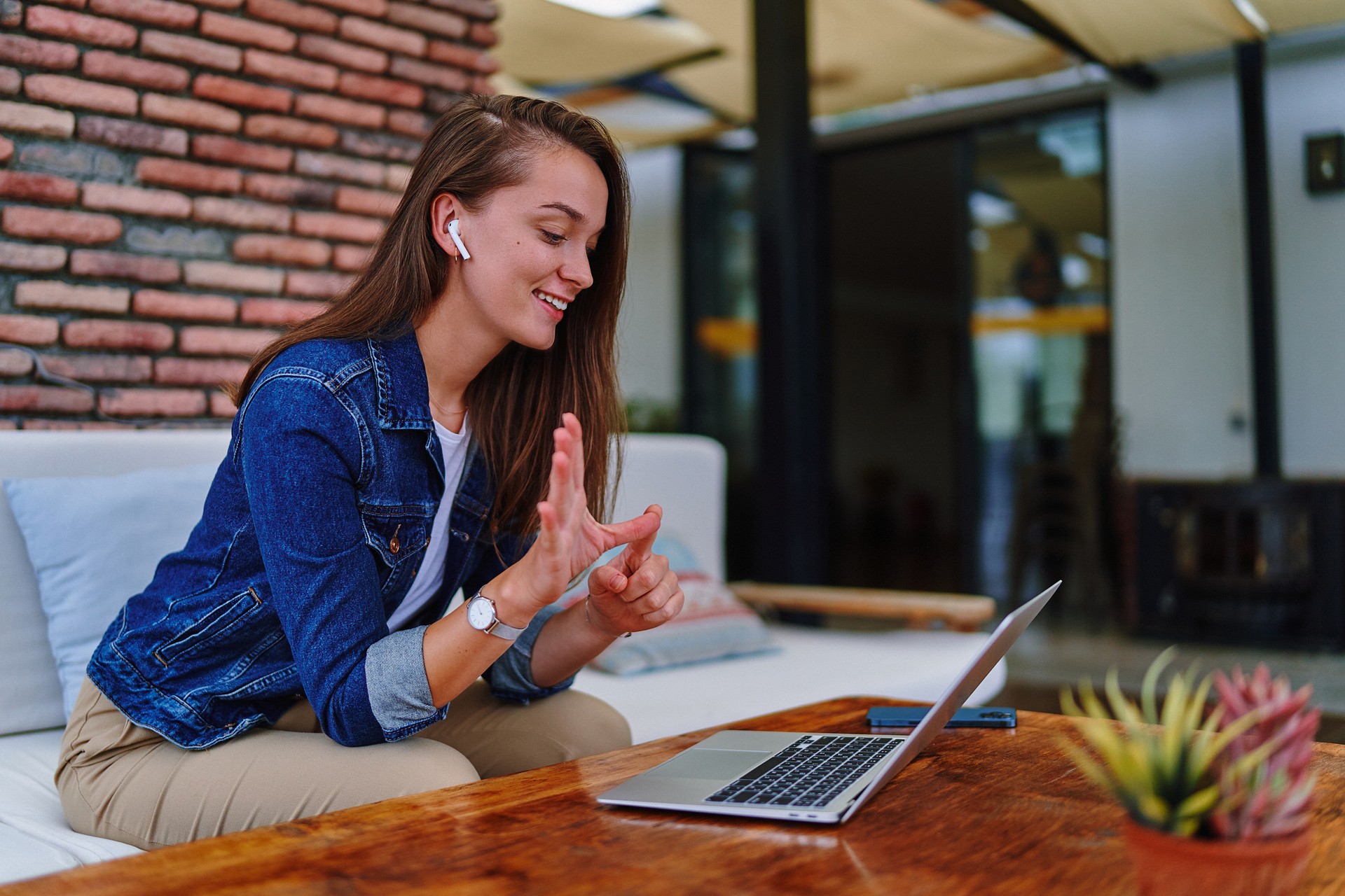 Cute young happy modern casual female using laptop for teaching sign language, video call, conference and online chatting webinar at cafe